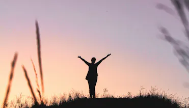 personne qui temps les bras vers le ciel pendant un coucher de soleil