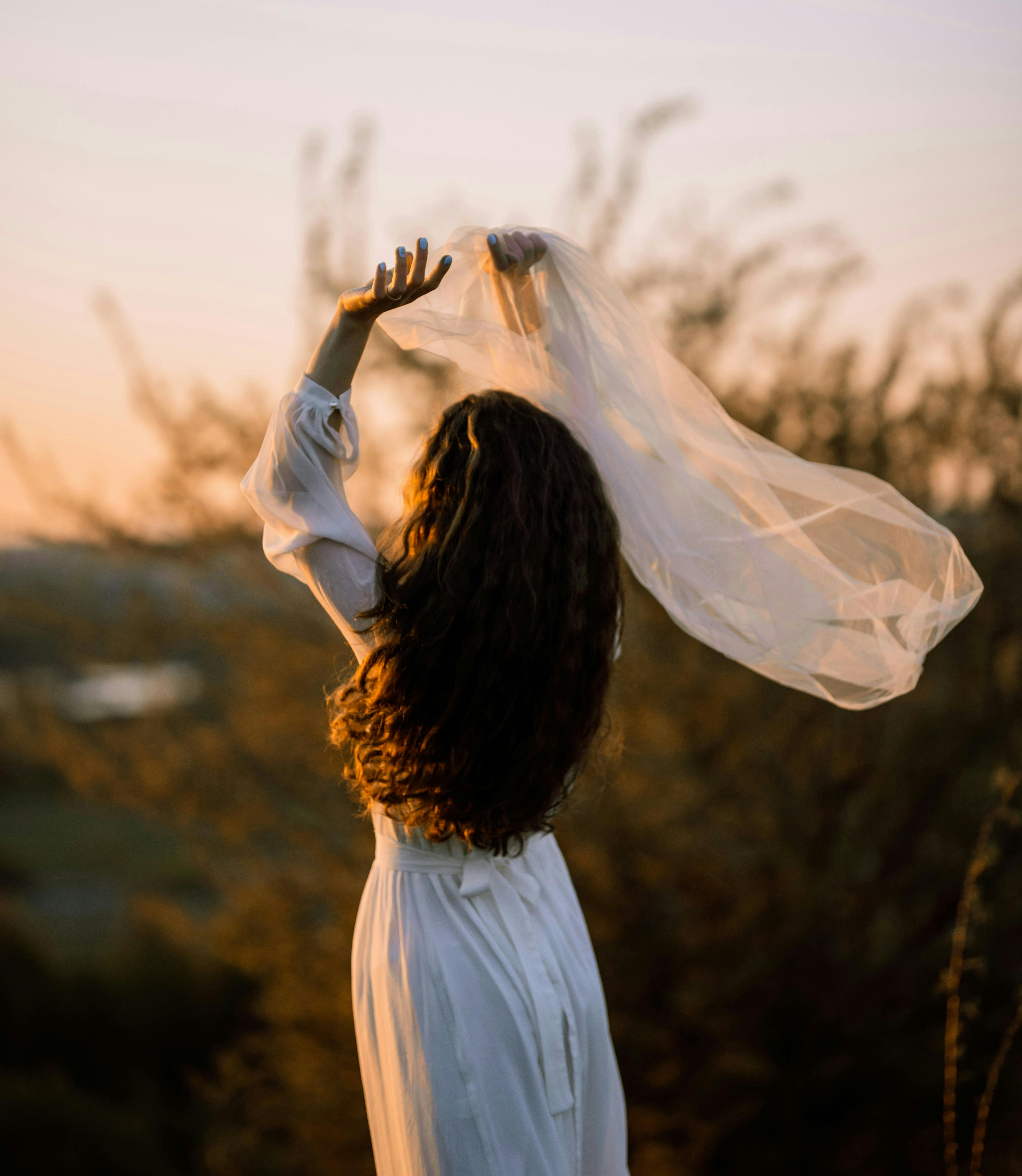 femme avec voile blanc au vent dans les mains et coucher de soleil