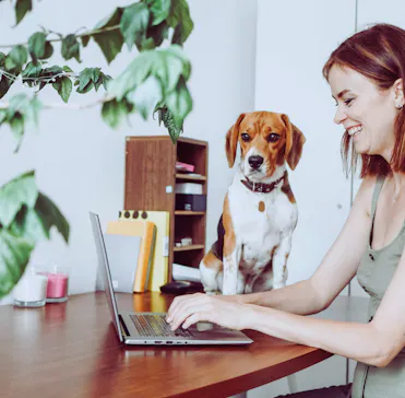 femme assise devant son ordinateur qui sourit avec son chien assis sur la table