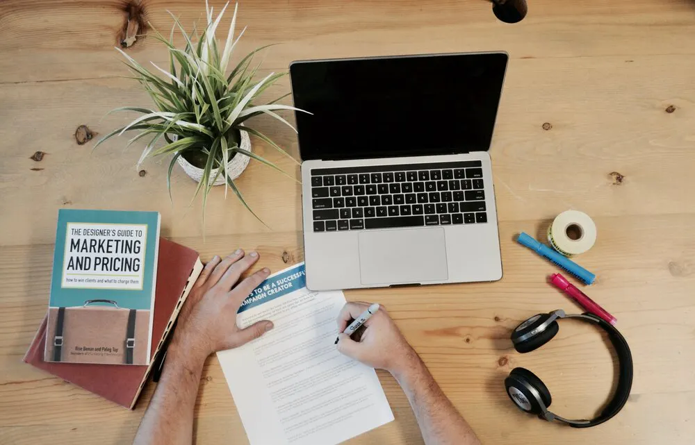 laptop on table with marketing plan and book