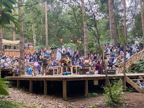 a large group of people in a forest watching a performance on stage