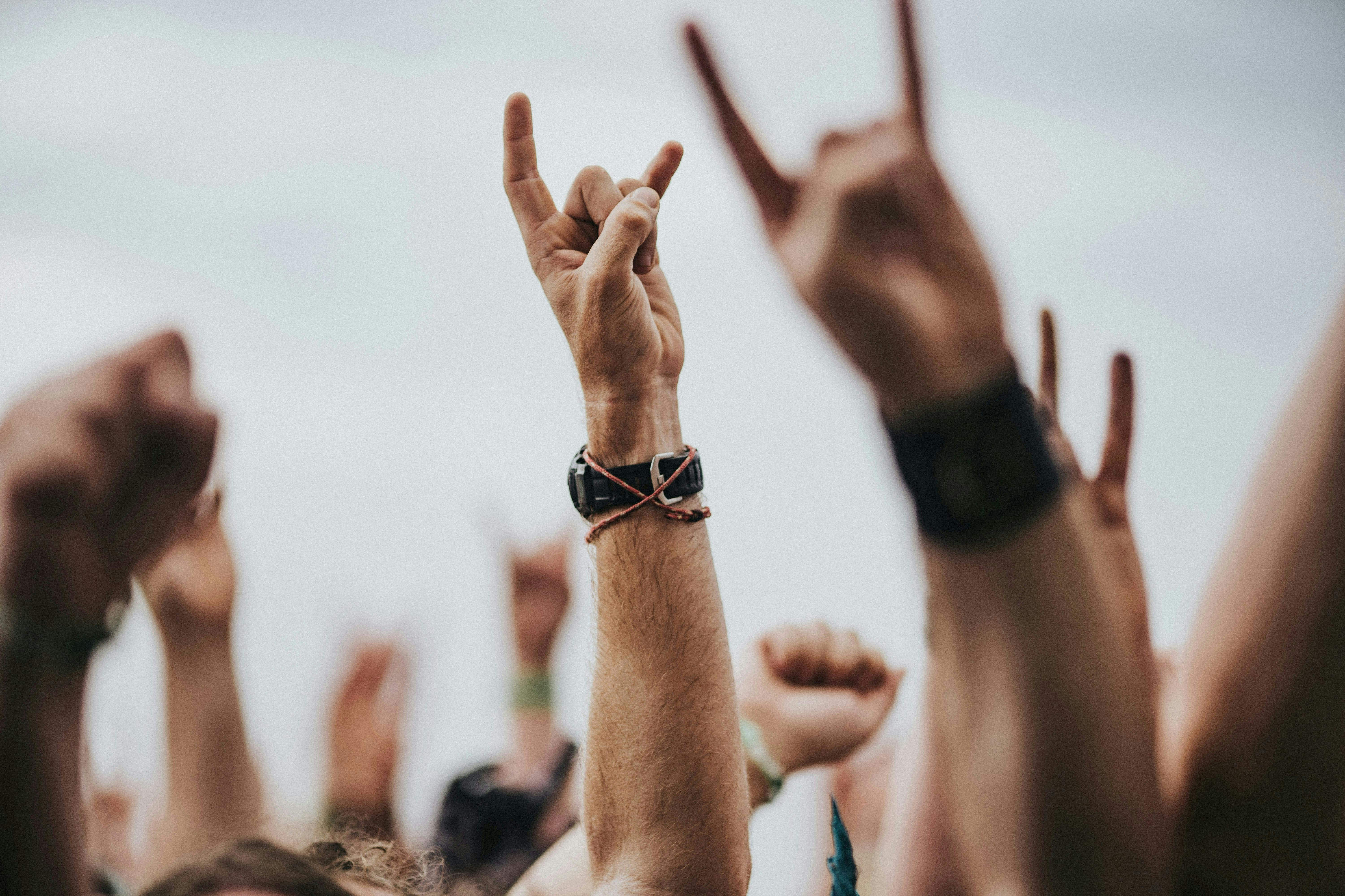 A close-up of raised hands in an audience making the sign of the horns
