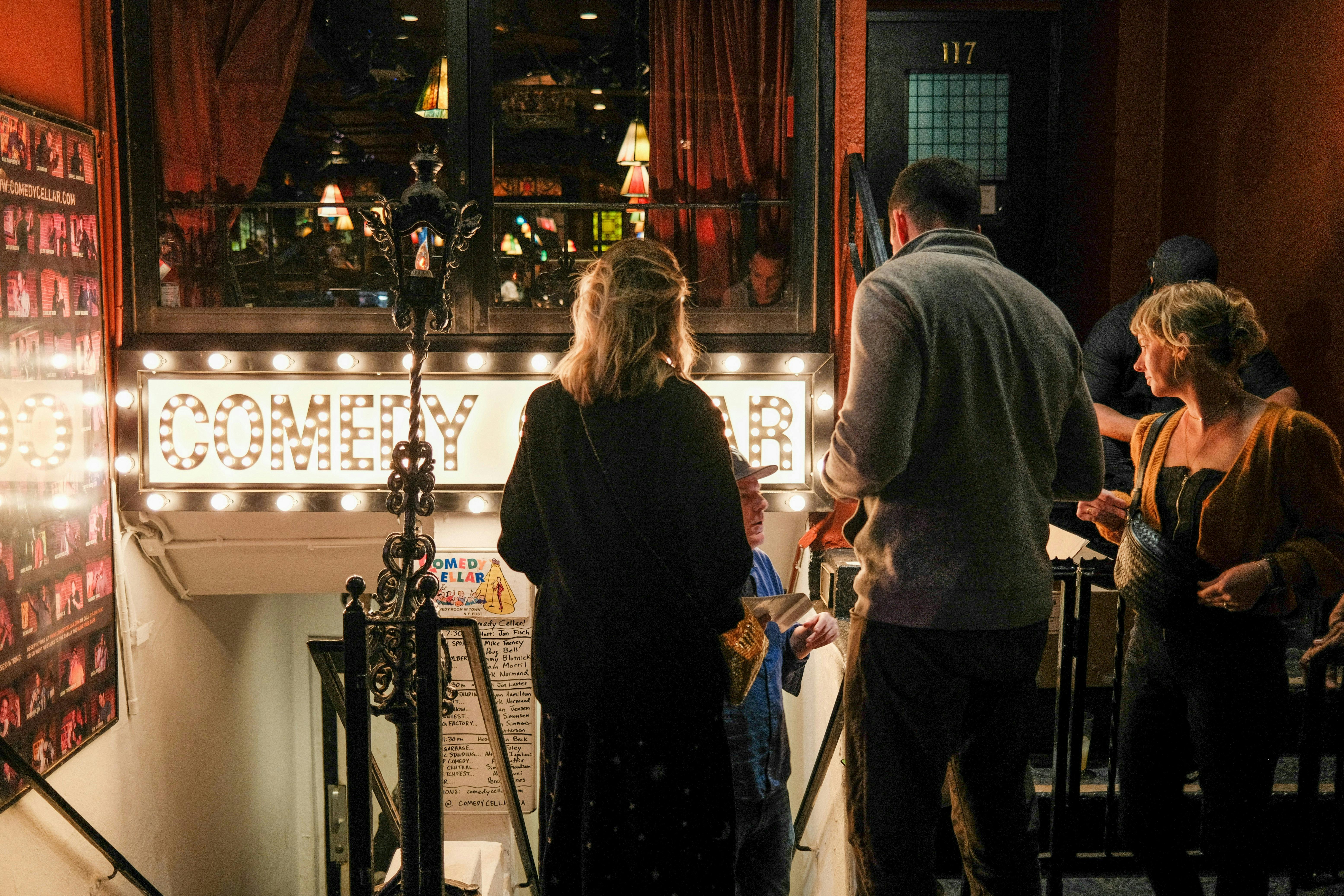 People entering a comedy club – dimly lit venue with brightly lit 'Comedy Club' sign