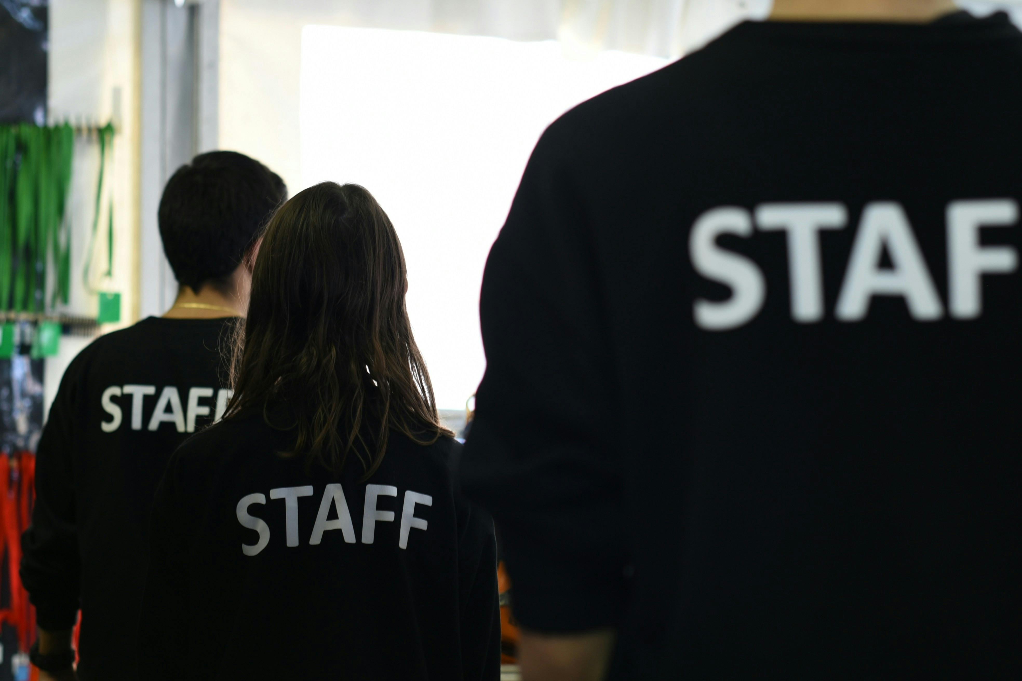 An image of three people wearing black t-shirts with the word 'staff' written on the back, taken from behind