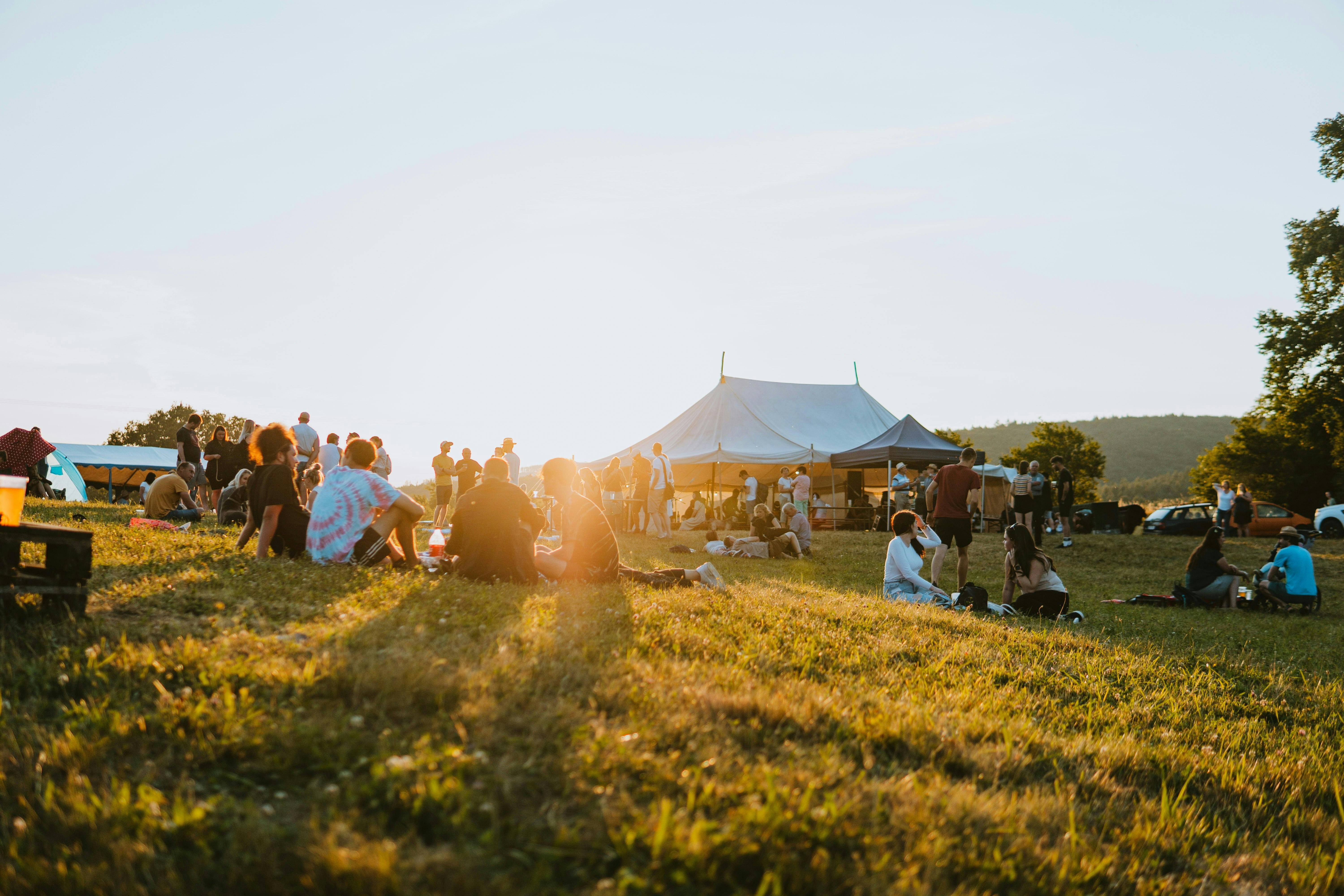 Field with people sitting on the floor at sunset and tents in the background
