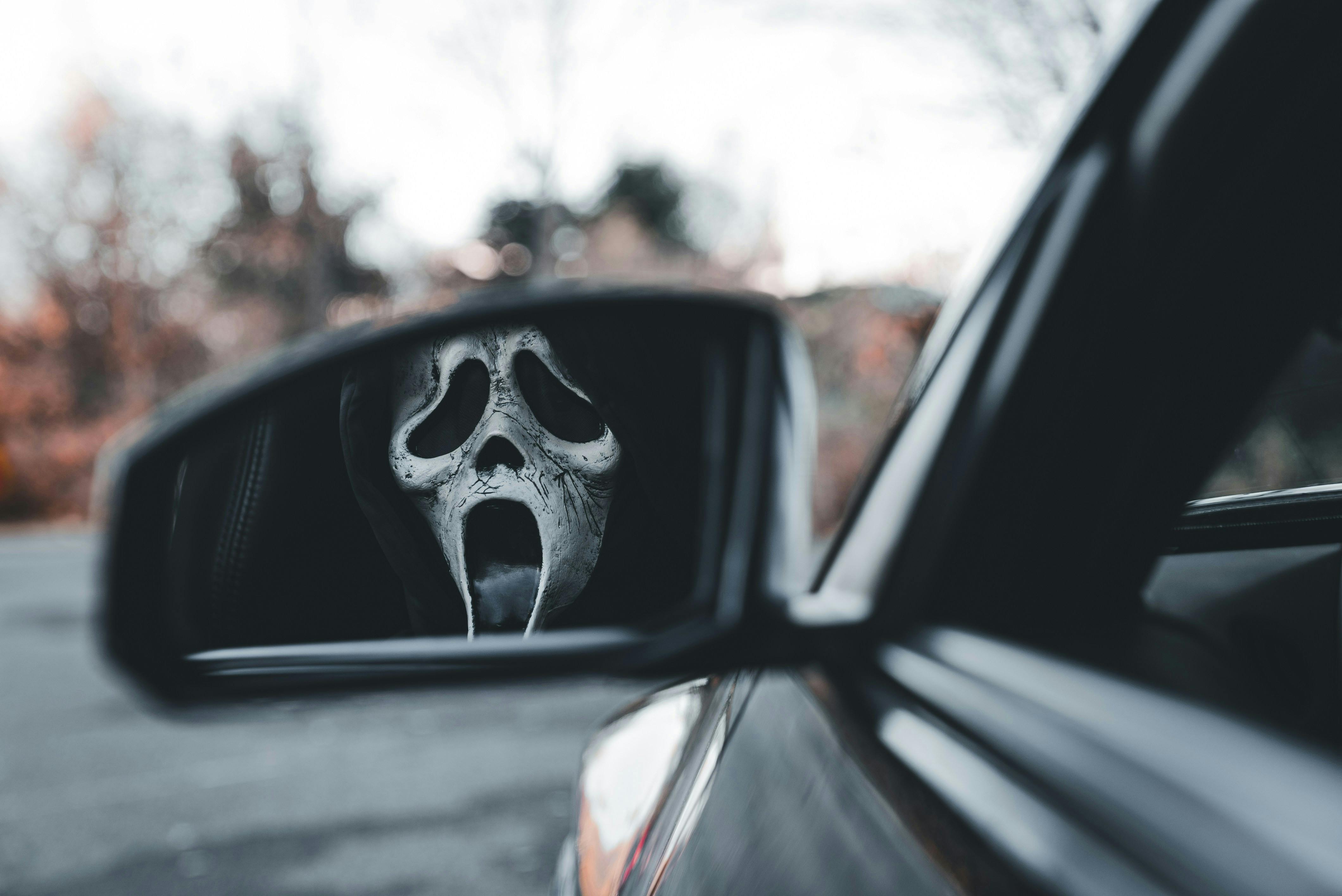 Car wing mirror showing reflection of Scream mask
