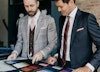 Two men in well made suits reviewing suit fabric swatches