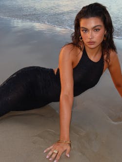 Model wearing a long black dress, laying on the sand on the beach