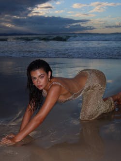 Model wearing a long gold dress, crawling on the sand on the beach