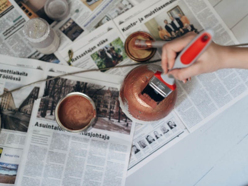 Open Paint Can with Copper Metallic Paint Inside and Hand Painting Pot on Newspaper Pages