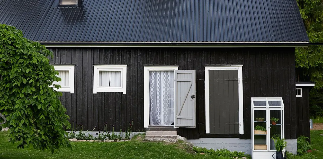 Wooden house with black walls and one door open.