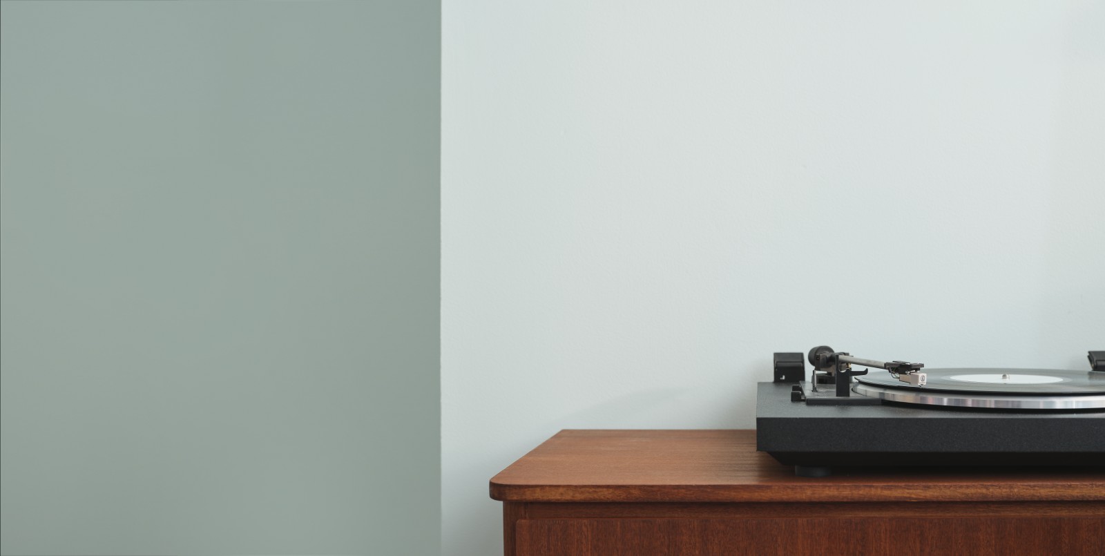 Close up view of wooden cabinet and record player against light green wall painted in shade crystal g371
