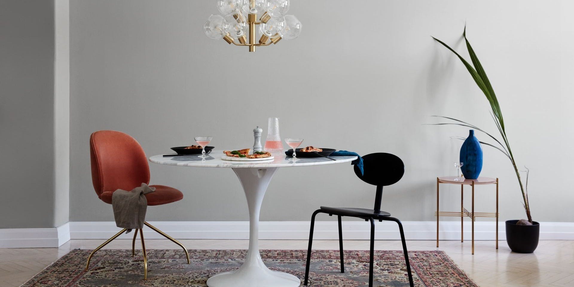 Light Grey Dining Room with Gold Chandelier, White Table, Orange Chair and Black Chair