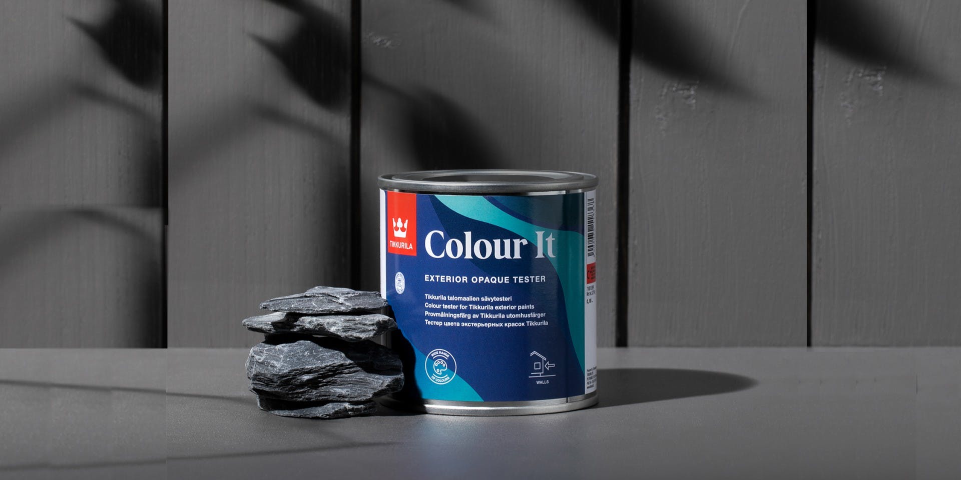 Close up of Colour It paint tester tin in front of grey wooden wall
