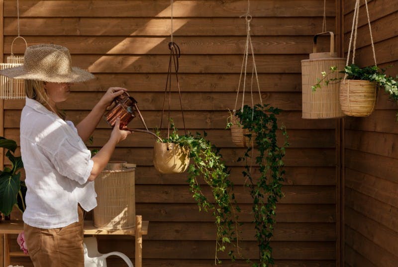 Woman Wearing Straw Hat Watering Hanging Plants