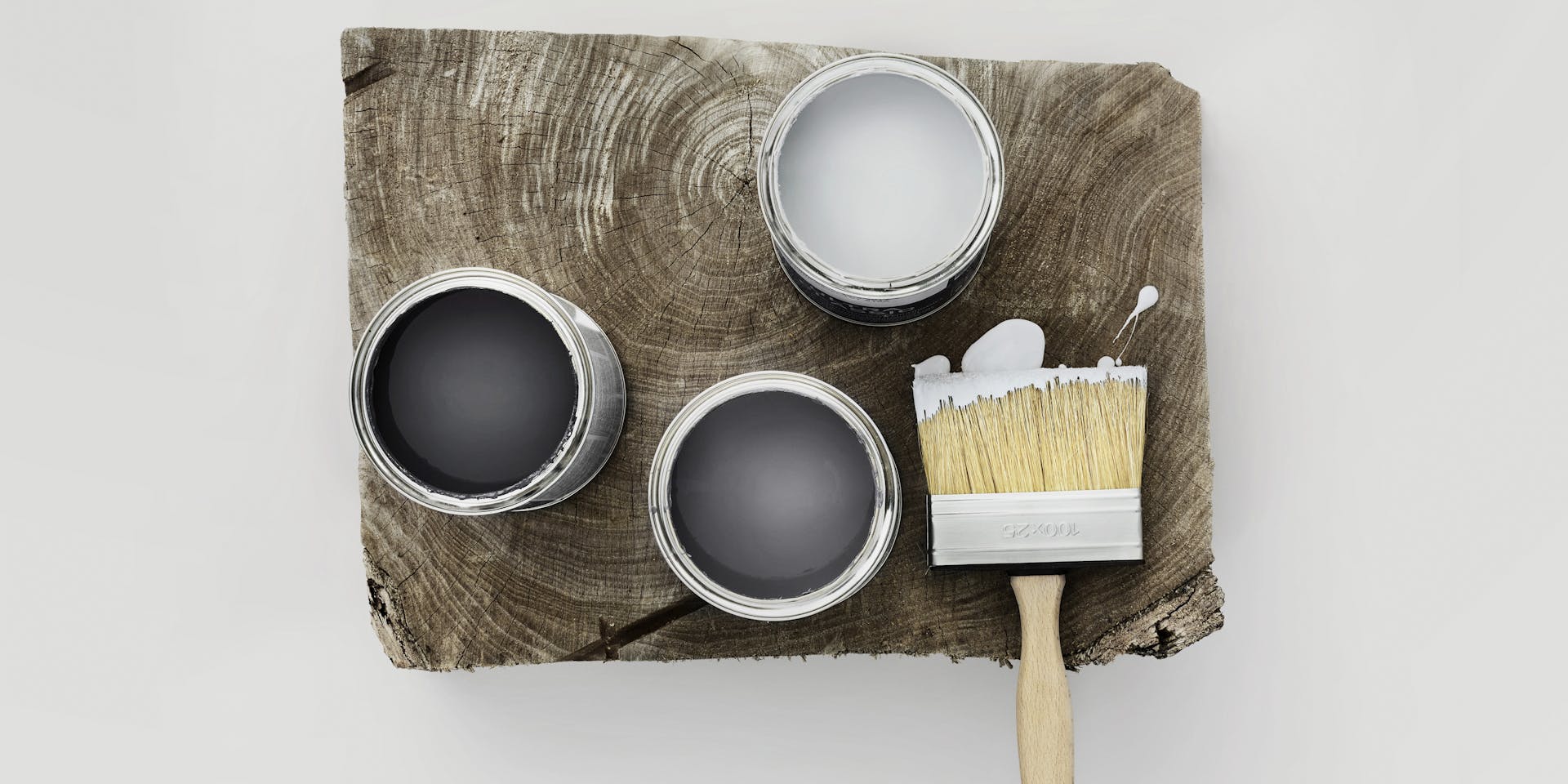 Three open cans with grey paint and paintbrush