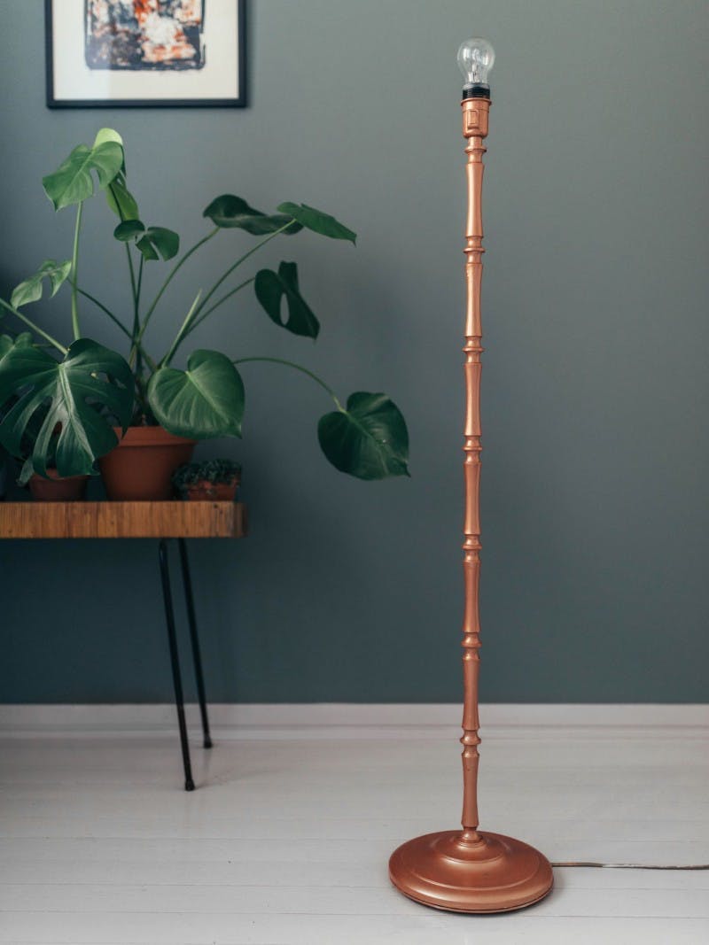 Plant on Stool, Painting and Copper Lamp Standing Against Green Wall 