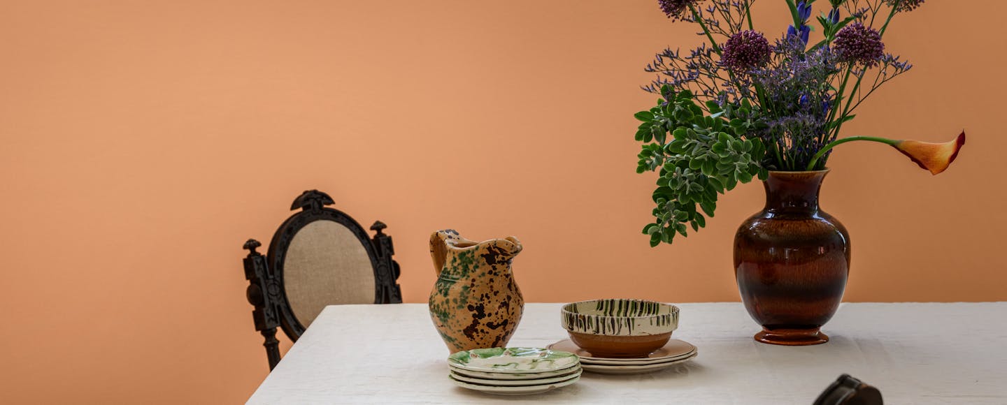 dining table with flowers and plates before orange wall