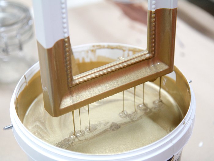 dipping white photo frame into tub of gold paint