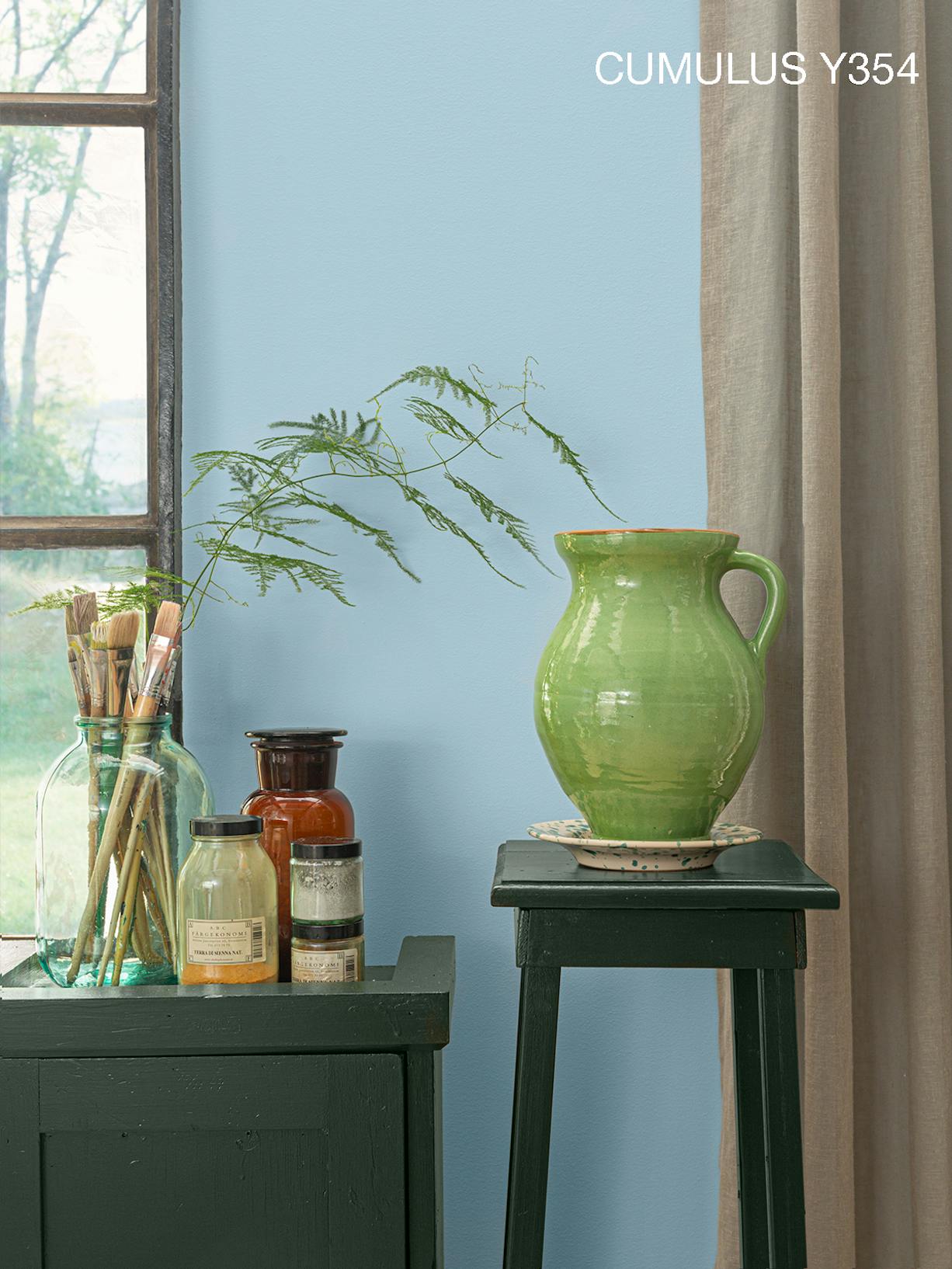 Decorations and Grey Vase on Black Stool Against Light Blue Wall