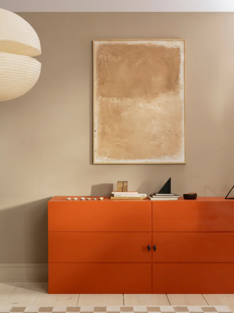 Orange painted sideboard against a warm neutral wall with abstract artwork
