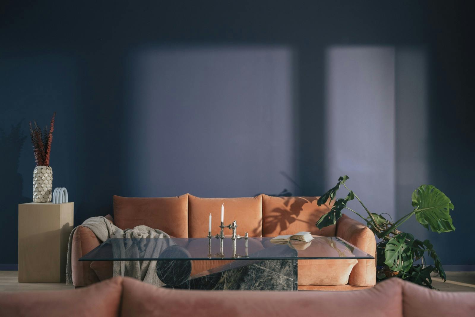 styled living room image with coral sofa, grey rug, plants and other interior sofas in front of blue painted wall