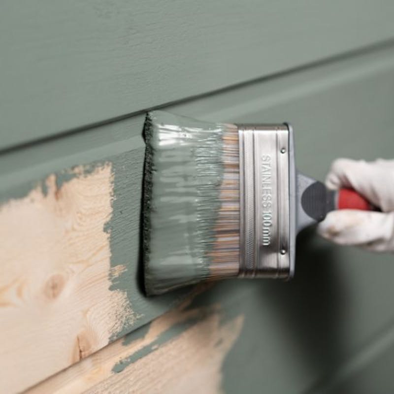 wooden fence being painted green with a large paint brush