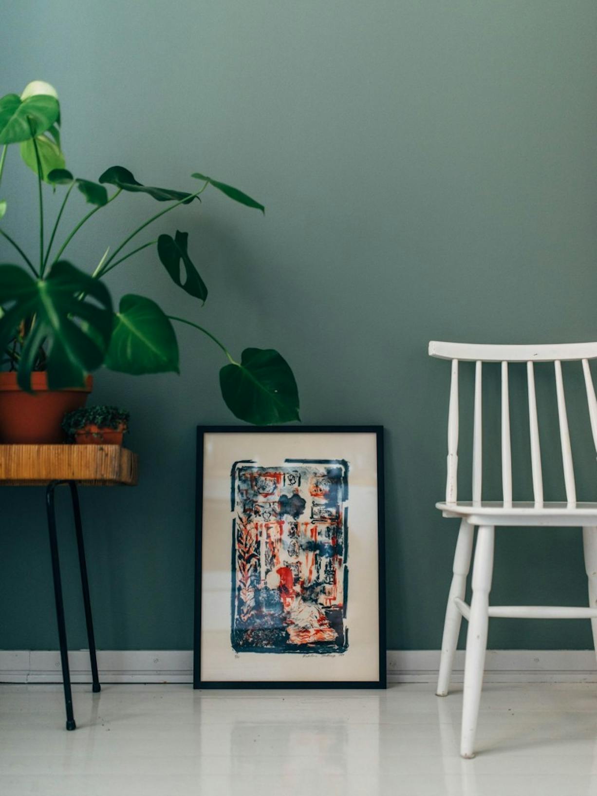 Plant on Stool, Painting and White Chair Standing Against Green Wall
