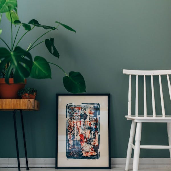 Plant on Stool, Painting and White Chair Standing Against Green Wall 