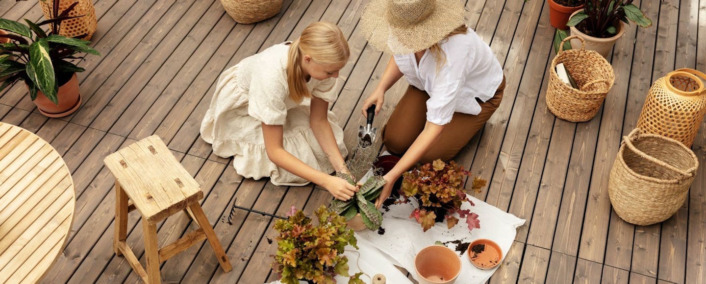 Woman Wearing Straw Hat and Girl Repotting Plants on Light Brown Terrace