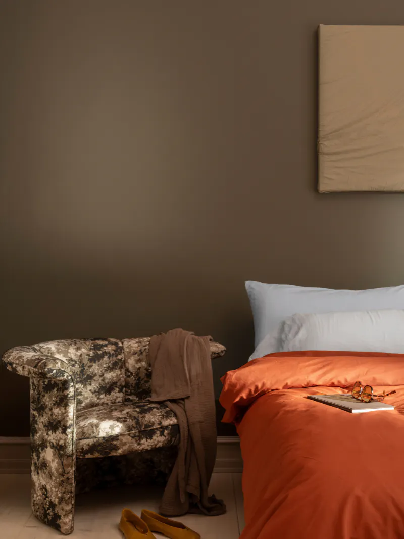 Bedroom with warm brown walls, orange bedding and patterned armchair