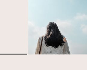 Photo of woman with black hair from behind and a blue sky.