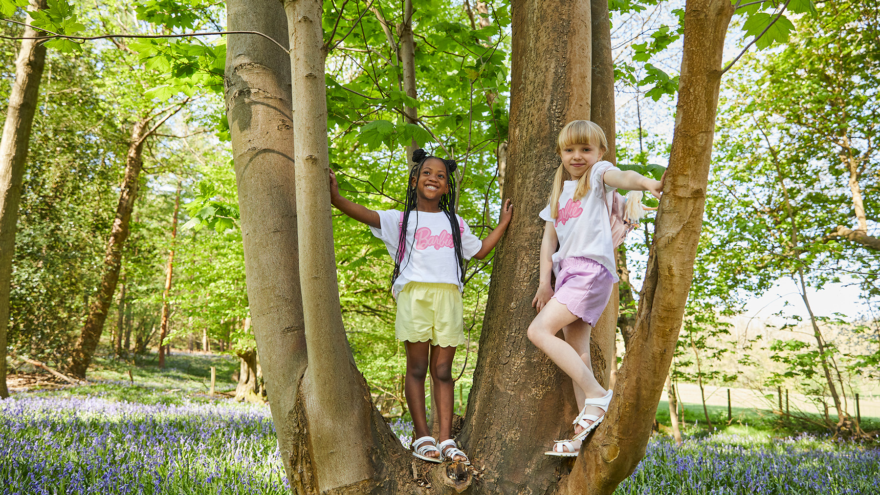 2 young girls pose for a photo in a tree, wearing matching barbie tshirts