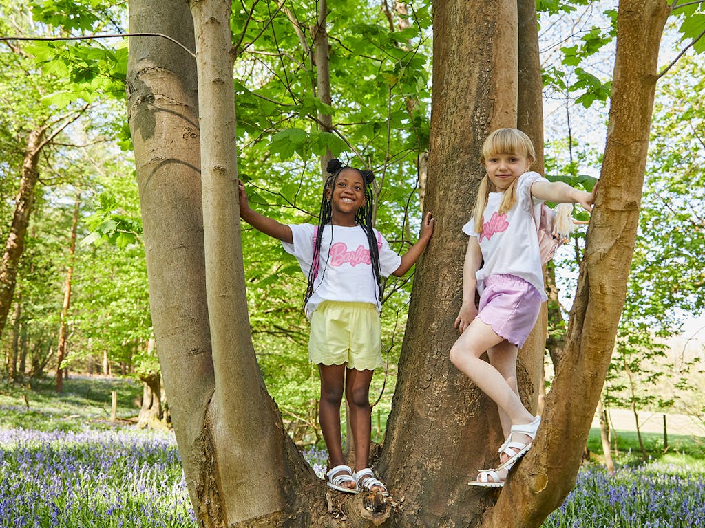 2 young girls pose for a photo in a tree, wearing matching barbie tshirts