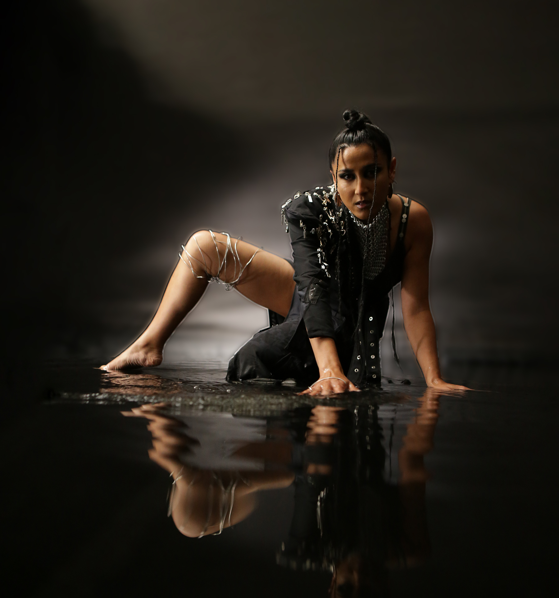 Edgy woman crawling through water dressed in navy fabric with silver chains