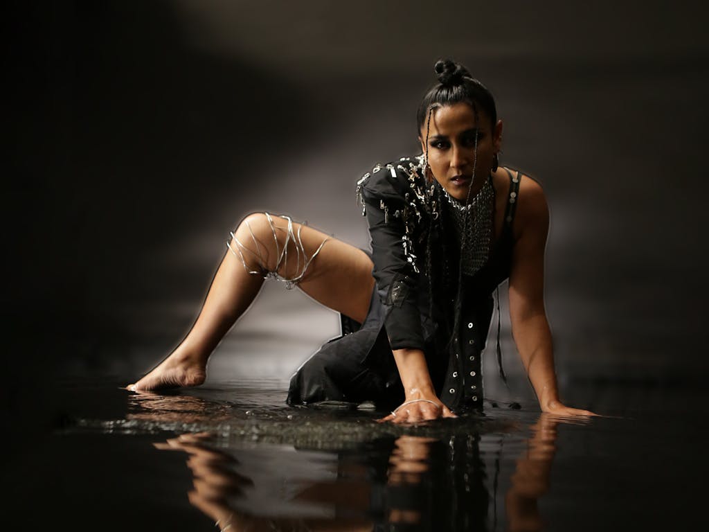 Edgy woman crawling through water dressed in navy fabric with silver chains