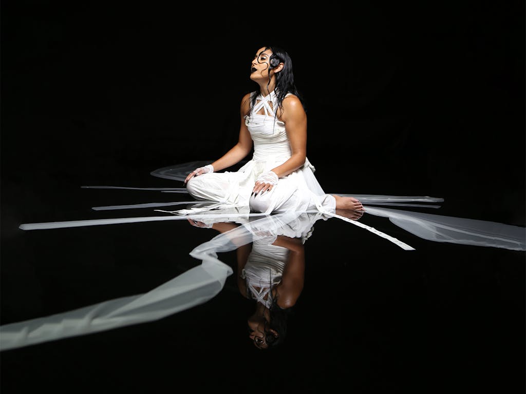 Fashion photography of a woman draped in long strips of white fabric in a black photography studio with water on the floor