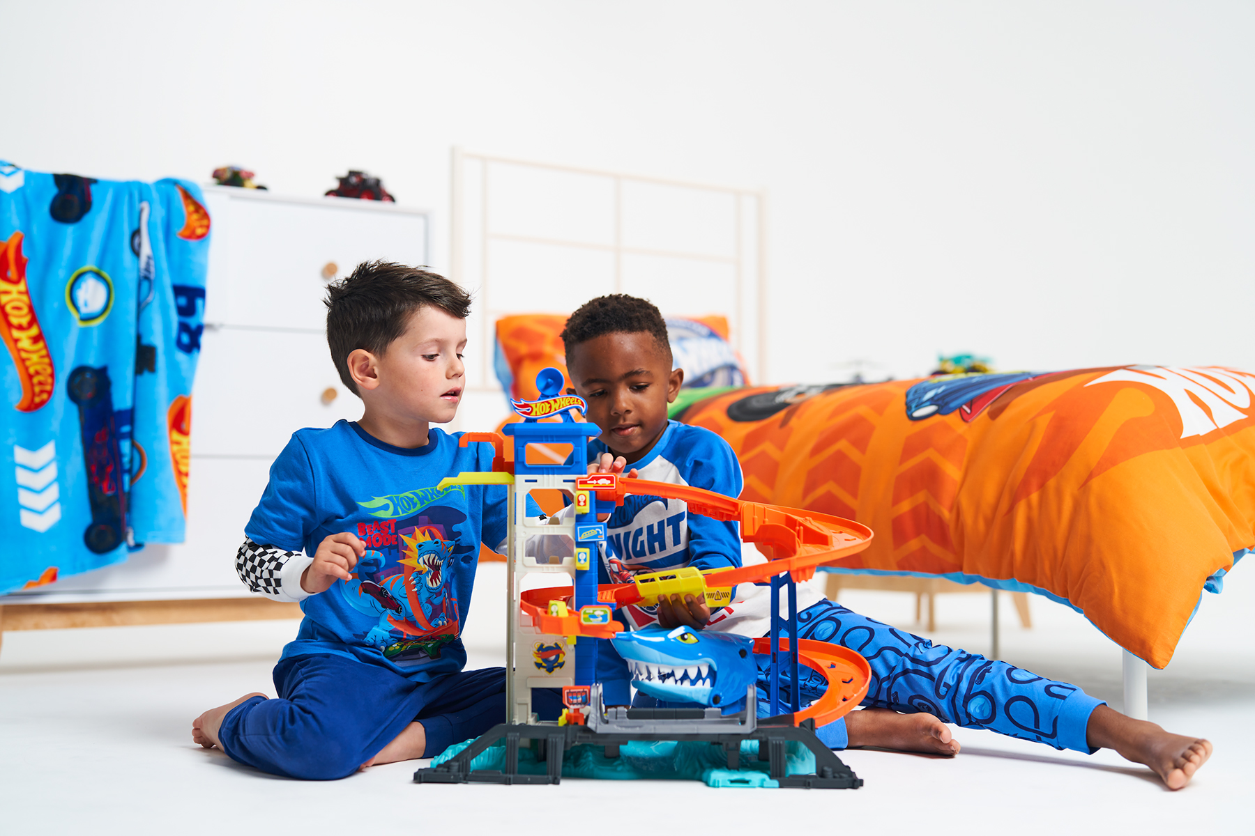 2 young boys play with a Hot Wheels race track, in a child's bedroom