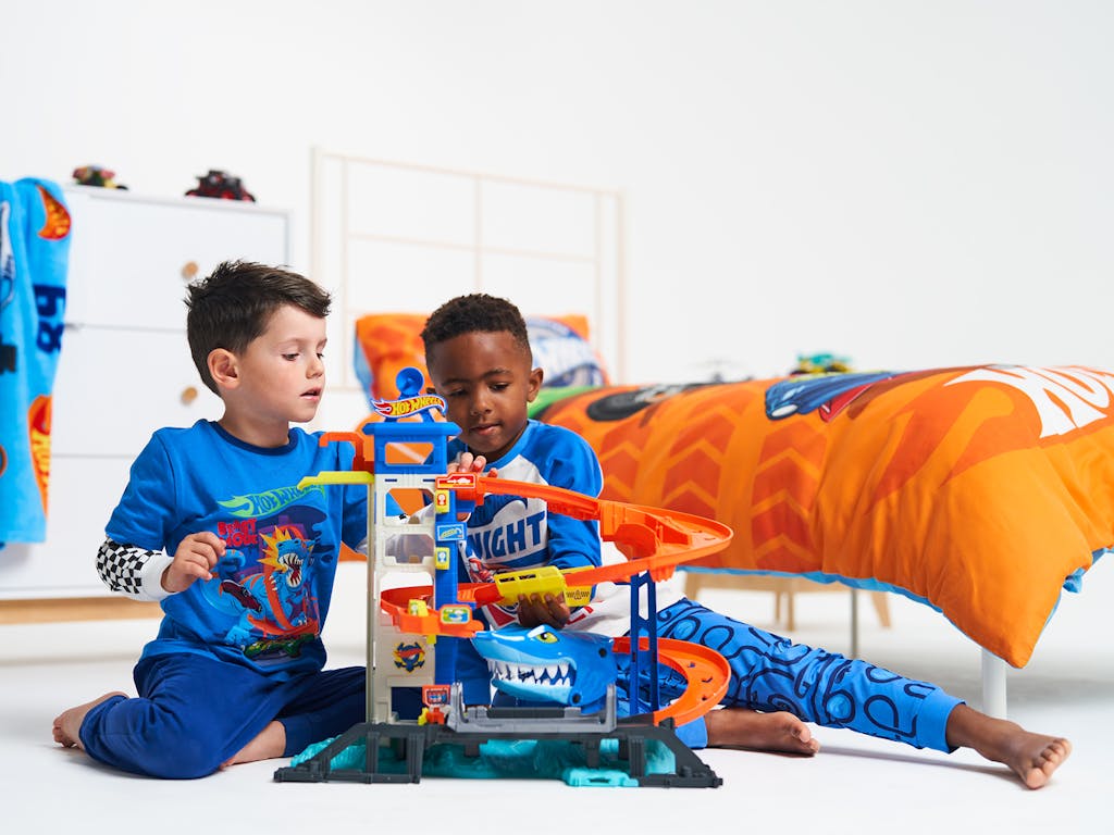 2 young boys play with a Hot Wheels race track, in a child's bedroom