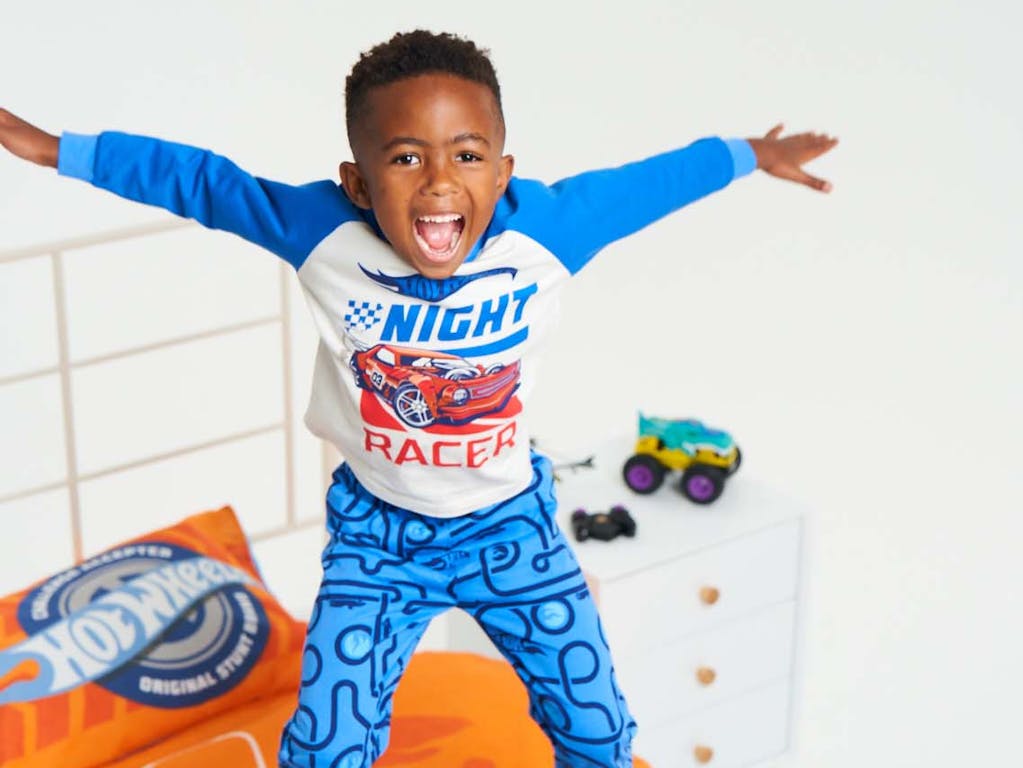 Young boy dressed in Hot Wheels pyjamas jumping on his Hot Wheels bed