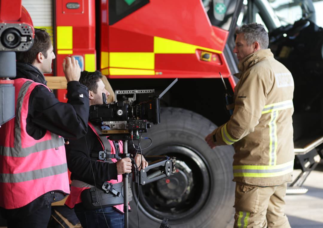 Two camera crew stood with a fireman in front of a fire engine