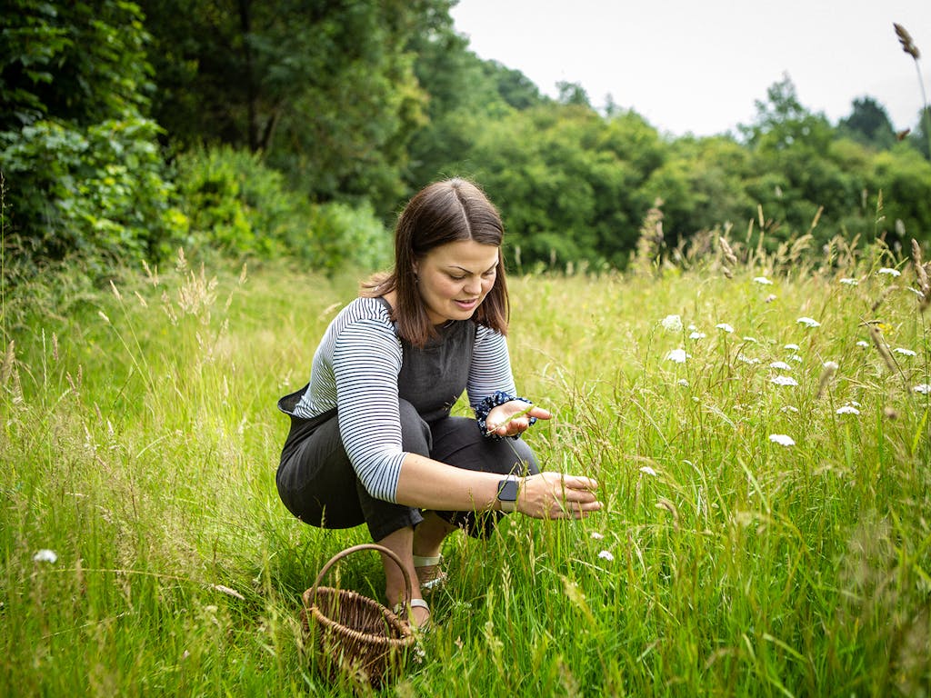 Lady crouches in a wild flower meadow to pick flowers