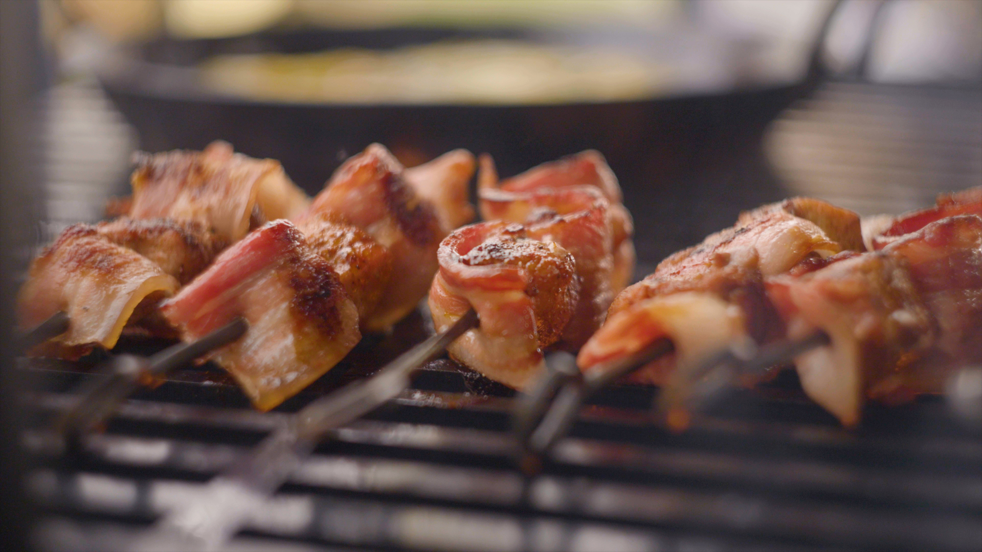 Crispy bacon and rabbit skewers cooking on a grill over fire
