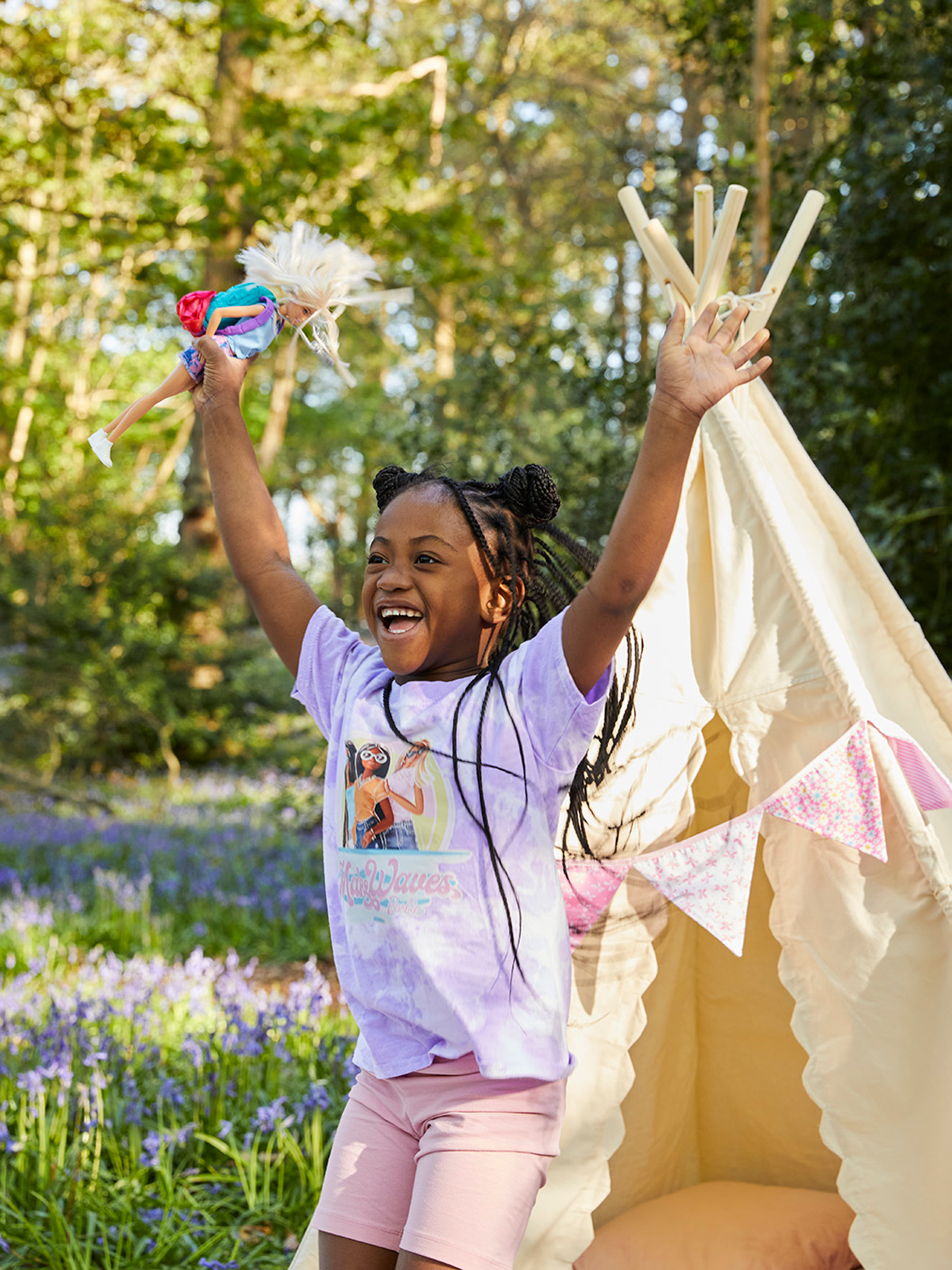 young girl in bluebell woodland jumps for joy with her barbie doll in hand