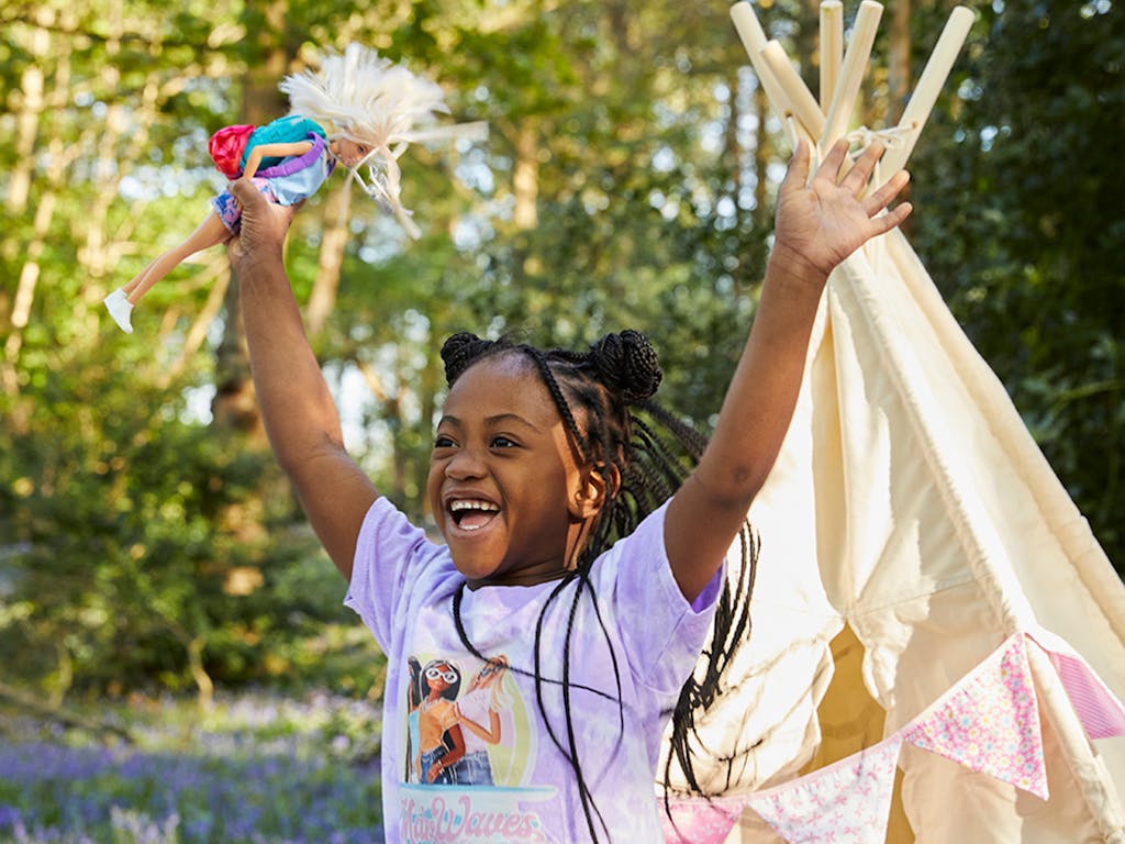 young girl in bluebell woodland jumps for joy with her barbie doll in hand