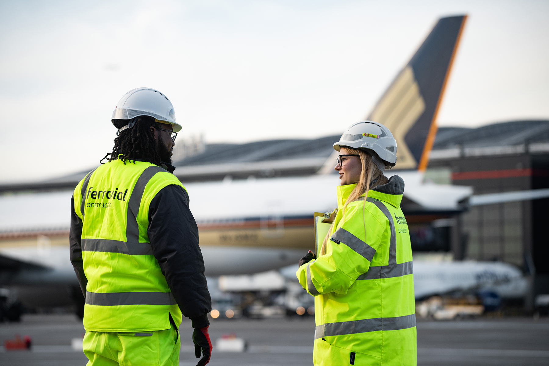 A man and a lady dressed in high-vis watching a plane take off