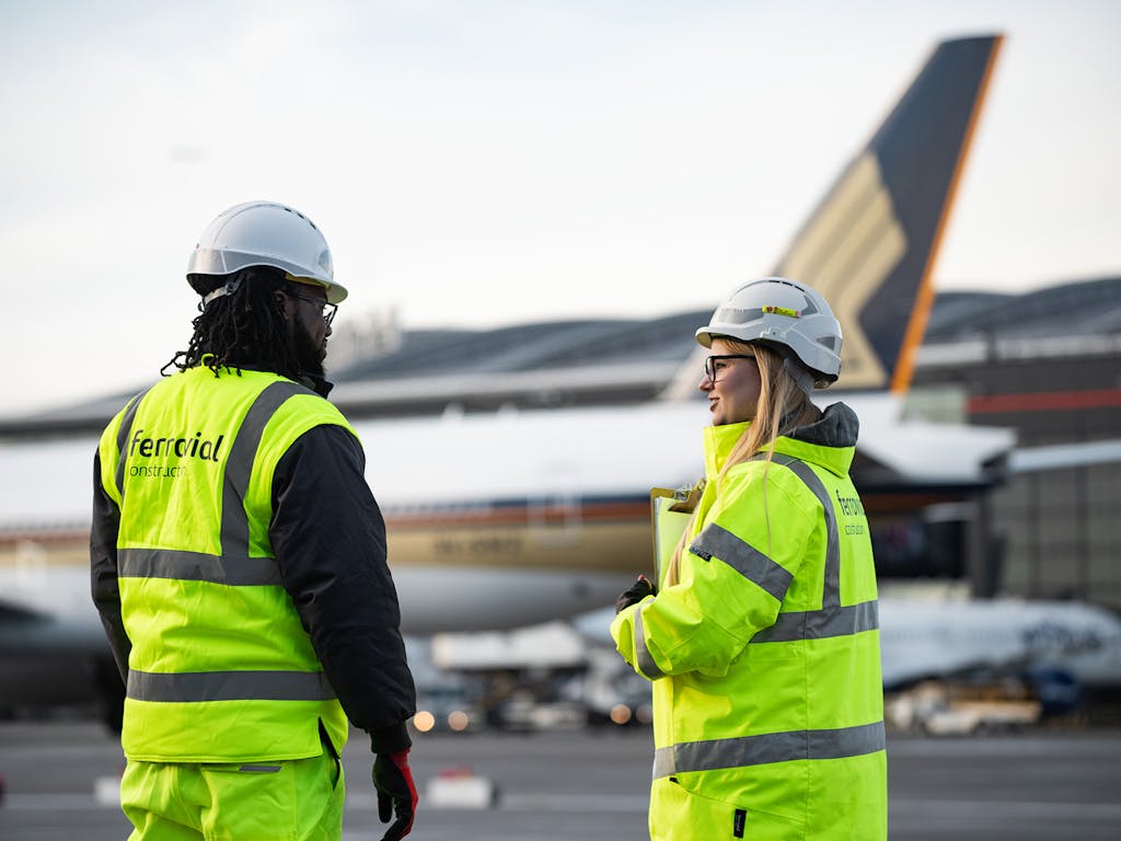 A man and a lady dressed in high-vis watching a plane take off