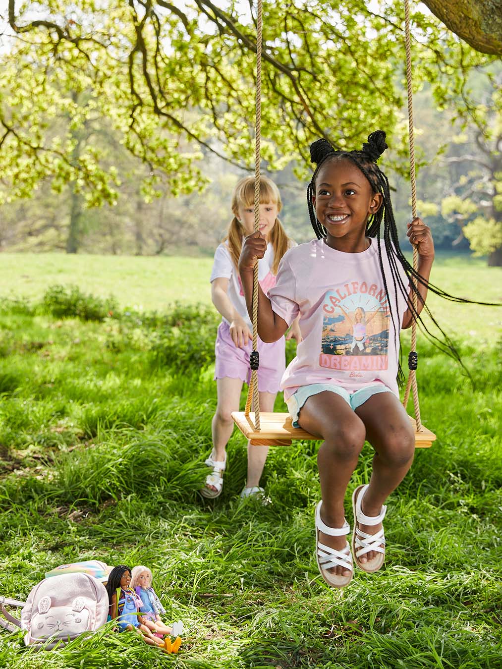 A young gilr pushes her friend on a swing dressed in Barbie T shirts