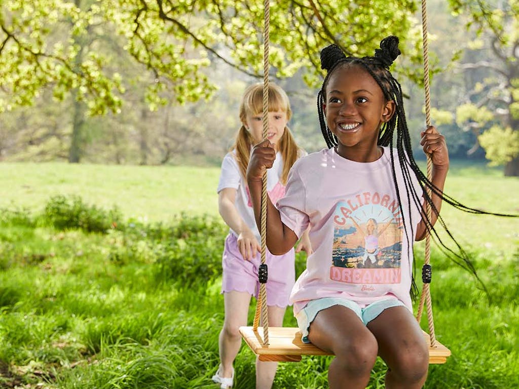 A young gilr pushes her friend on a swing dressed in Barbie T shirts