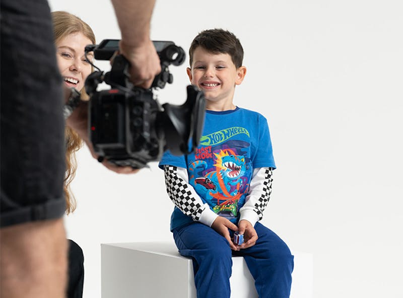 Young boy dressed in Hot Wheels pyjamas smiles for a video camera